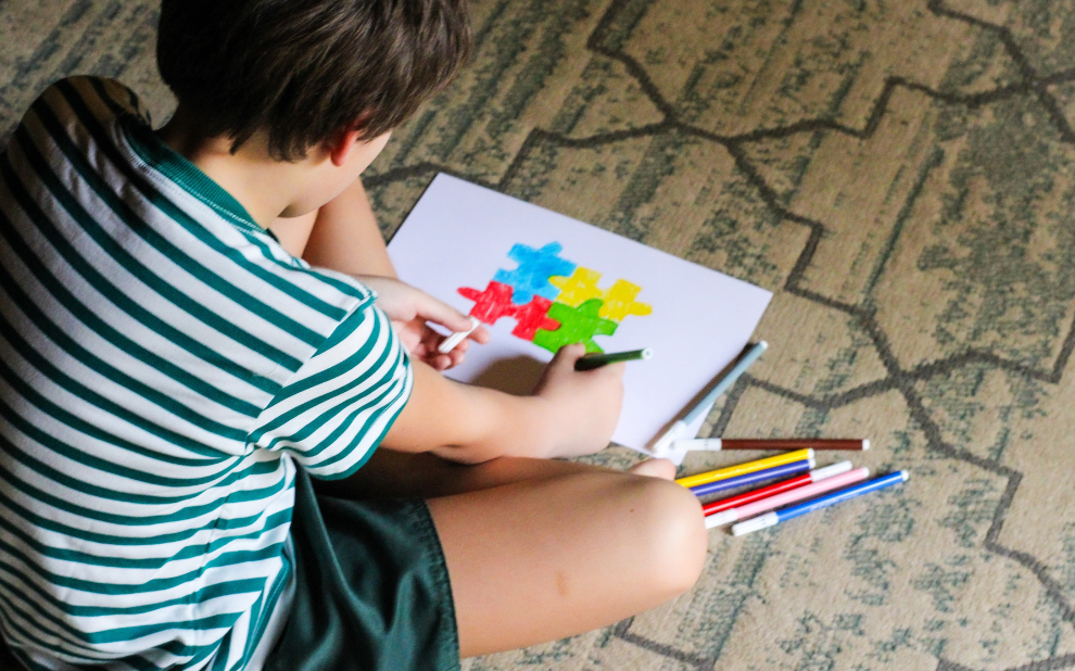 Imagem criança sentada desenhando símbolo do autismo