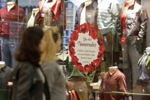 Imagem duas mulheres olhando para uma estante com roupas e um cartaz do dia dos namorados
