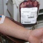 Imagem Doação de Sangue. Cateter está retirando sangue de uma pessoas, bolsa de sangue aparece cheia ao fundo.