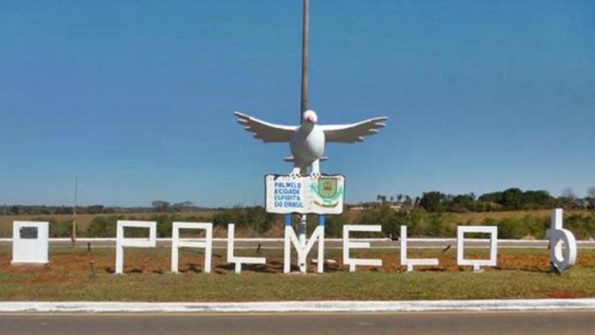 Imagem letreiro na entrada da cidade com o nome PALMELO em cima uma placa e uma pomba branca