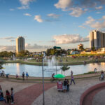 A imagem mostra o Parque Ipiranga, lago, pessoas e prédios em volta