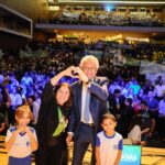 Imagem governador Ronaldo Caiado e secretaria de Educação Fátima Gavioli. ao lado de duas crianças, ao fundo alunos de rede estadual de educação.