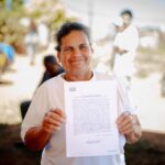 Imagem senhora segurando escritura, ela está sorrindo e olhando para a câmera.
