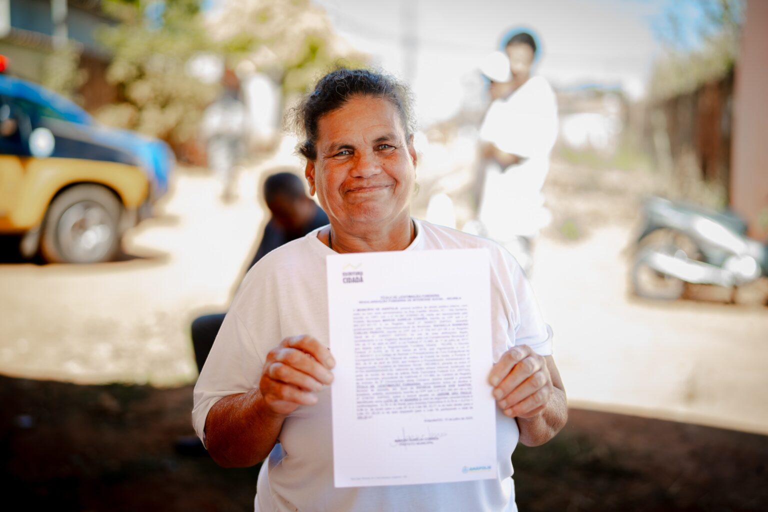 Imagem senhora segurando escritura, ela está sorrindo e olhando para a câmera.