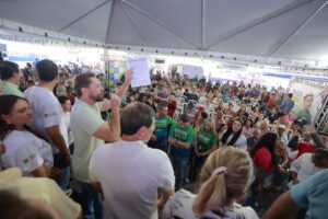 Imagem vários pessoas em evento da Alego, ao centro um homem fala com microfone na mão