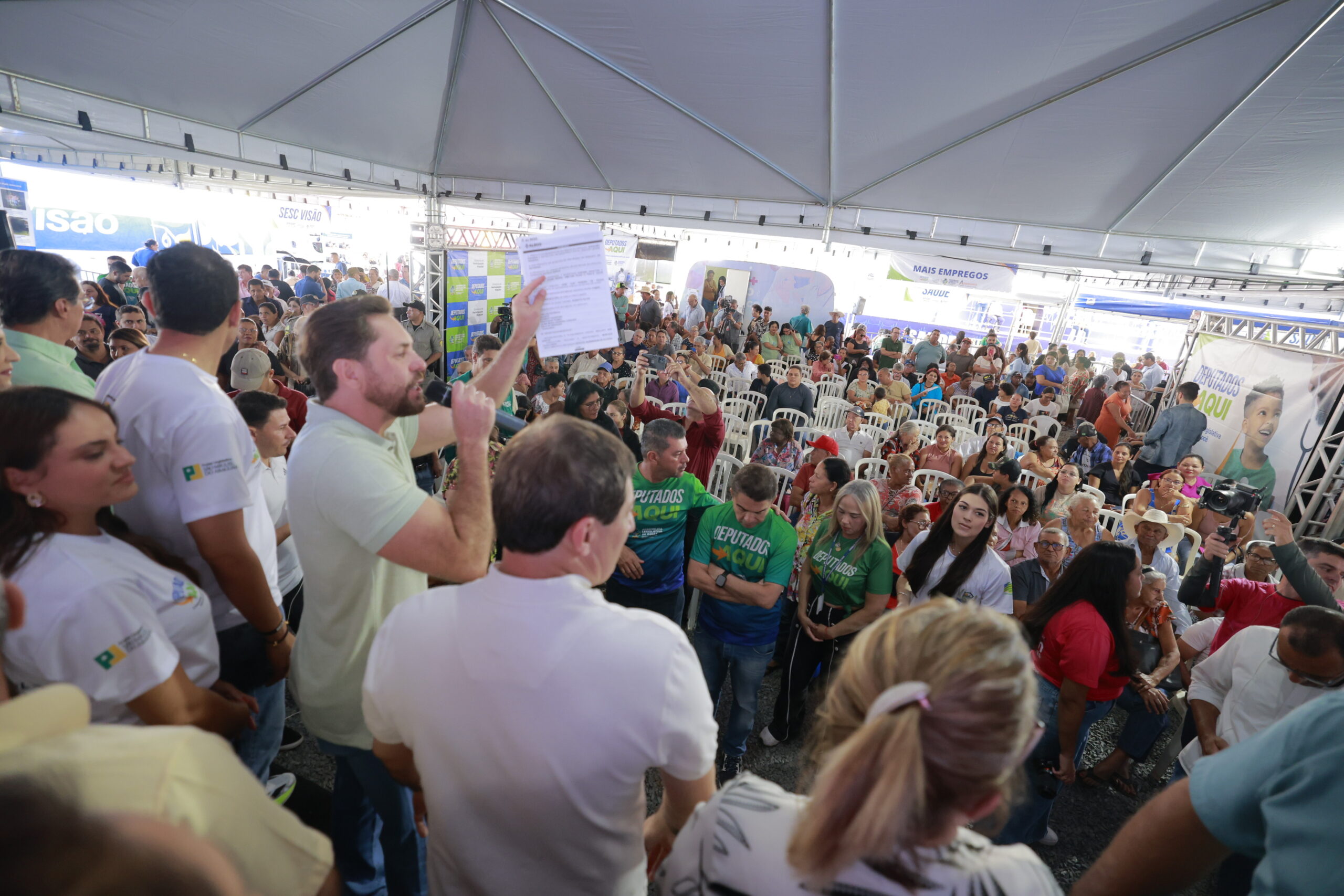 Imagem vários pessoas em evento da Alego, ao centro um homem fala com microfone na mão