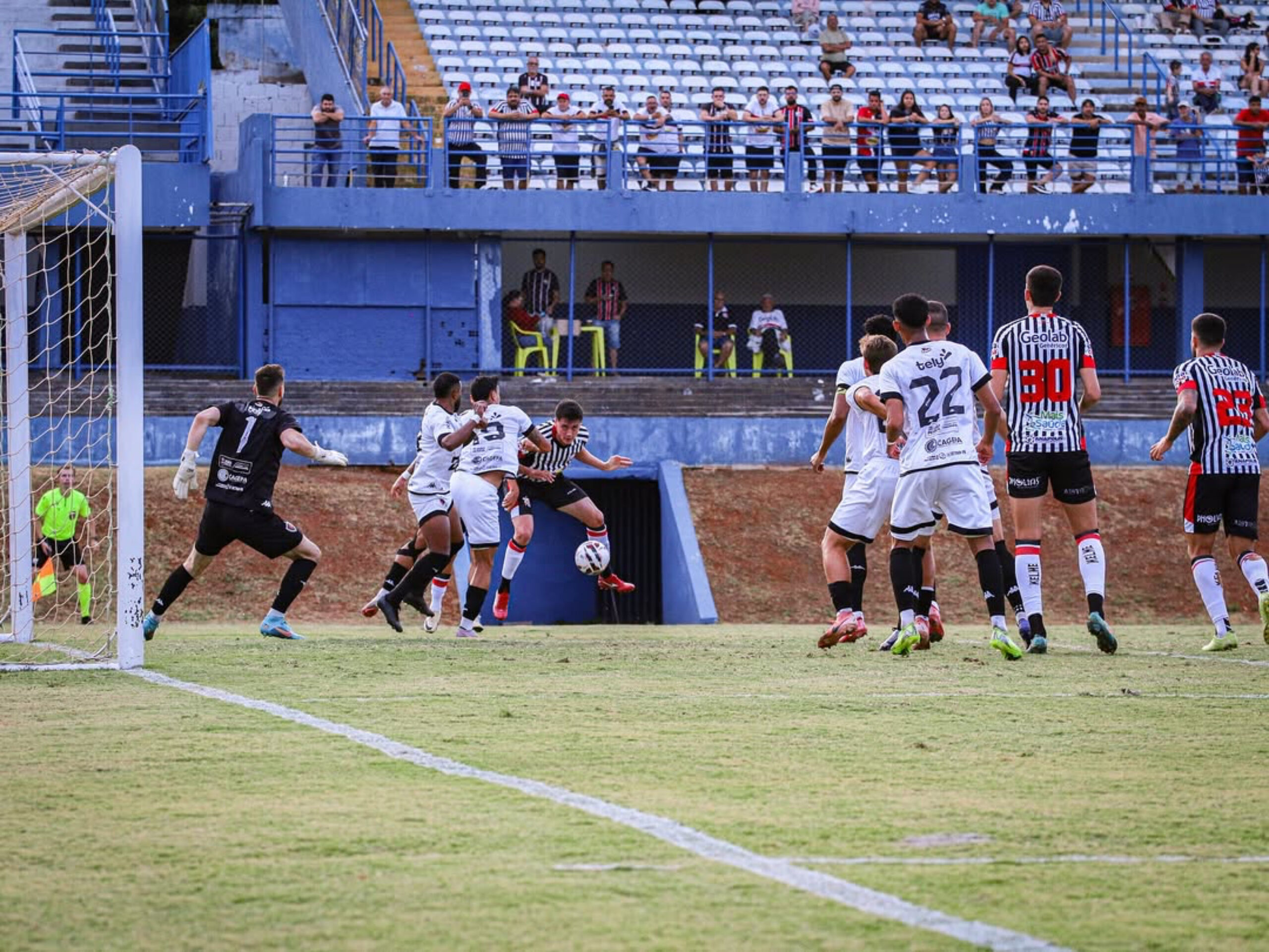 Imagem jogadores Anápolis x Botafogo-PB, um jogador do Anápolis chuta a bola e jogadores dos dois times estão dentro da área.