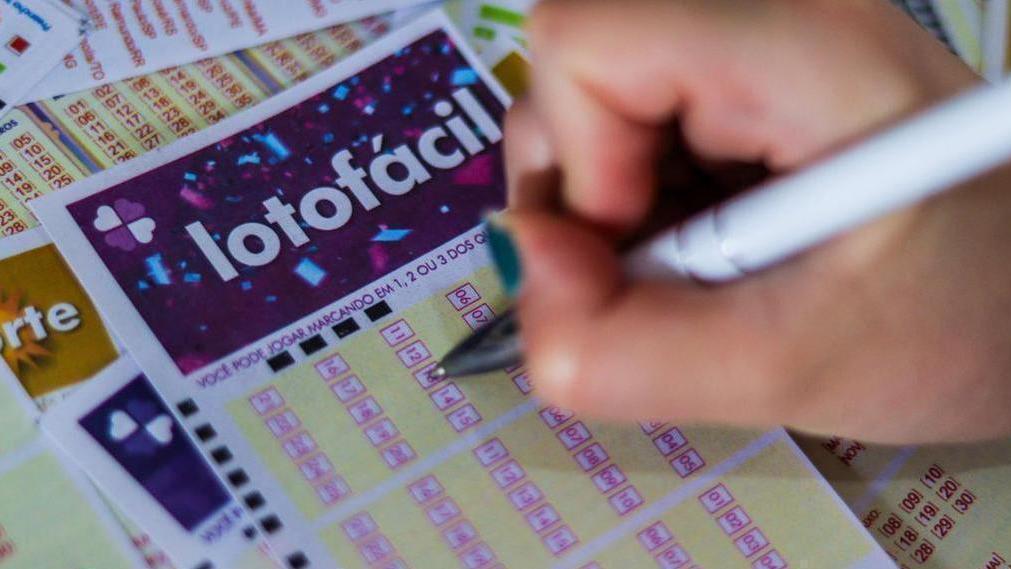Imagem uma mão segurando uma caneta e preenchendo jogo da lotofacil
