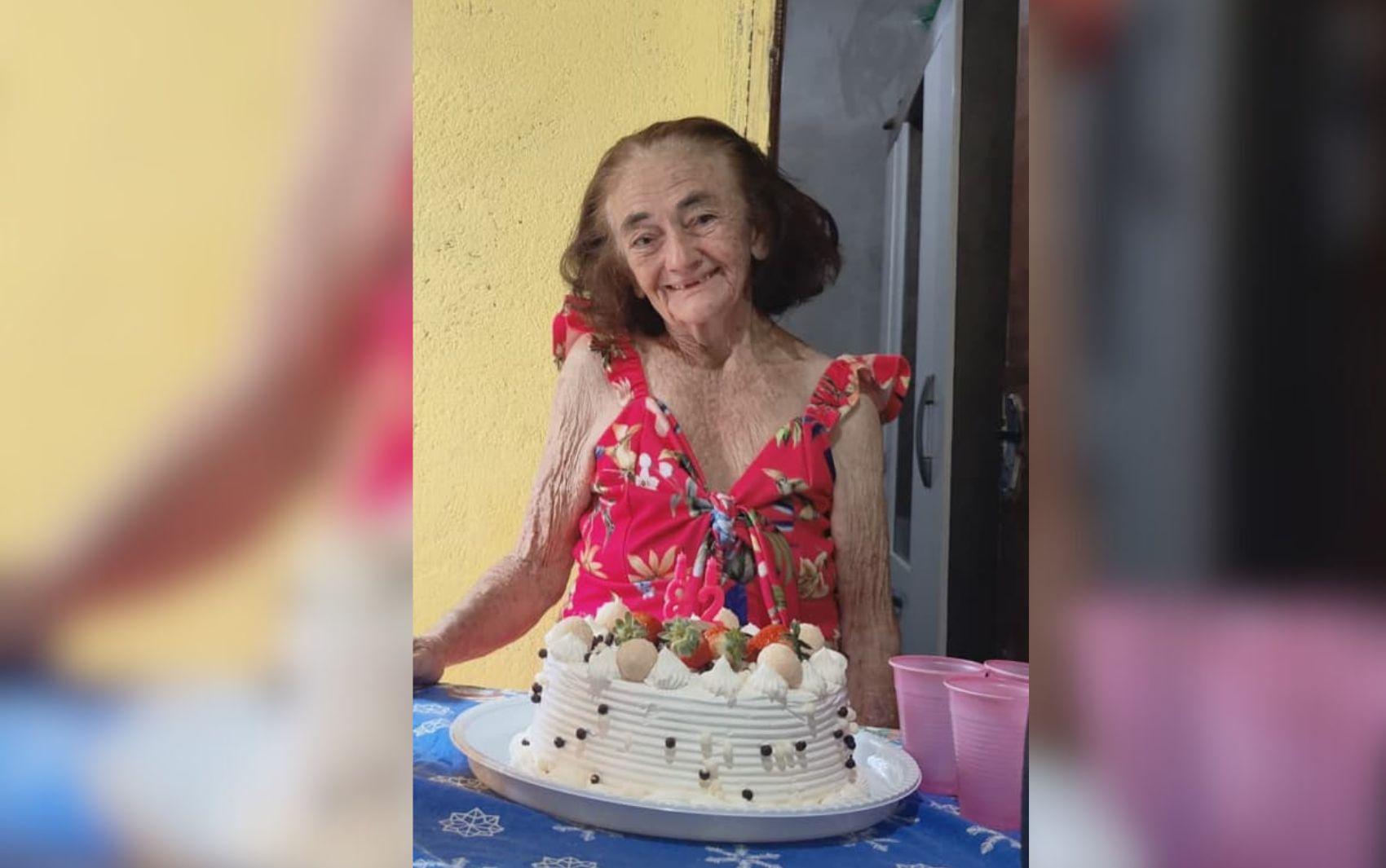 Imagem Idosa Desaparecida, ela está sorrindo com um bolo de aniversário na mesa