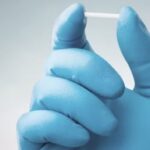 Imagem uma mão com luva azul, segurando um material para implante