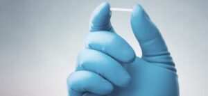 Imagem uma mão com luva azul, segurando um material para implante