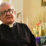 Imagem Padre Joaquim, vestido de batina preta ao lado tem imagens de santos