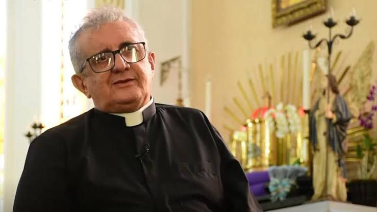 Imagem Padre Joaquim, vestido de batina preta ao lado tem imagens de santos