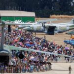 Imagem varias pessoas na Base Área de Anápolis, estão próximos a aviões grandes, pequenos e Caças da Força Aérea Brasileira