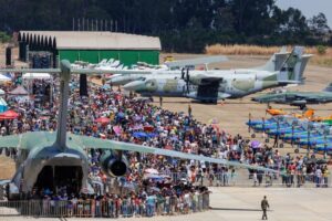 Imagem varias pessoas na Base Área de Anápolis, estão próximos a aviões grandes, pequenos e Caças da Força Aérea Brasileira