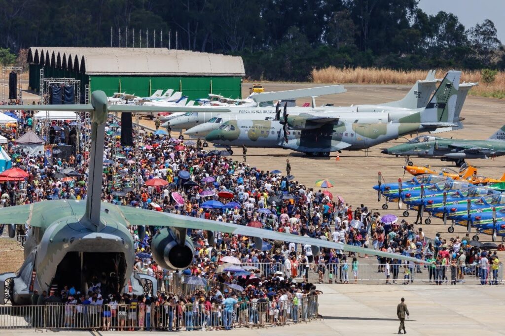 Imagem varias pessoas na Base Área de Anápolis, estão próximos a aviões grandes, pequenos e Caças da Força Aérea Brasileira