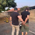 Imagem homem preso algemado com as mãos para traz, sendo conduzido por policial