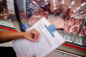 Imagem pessoa escrevendo na prancheta ao fundo carnes em um freezer transparente