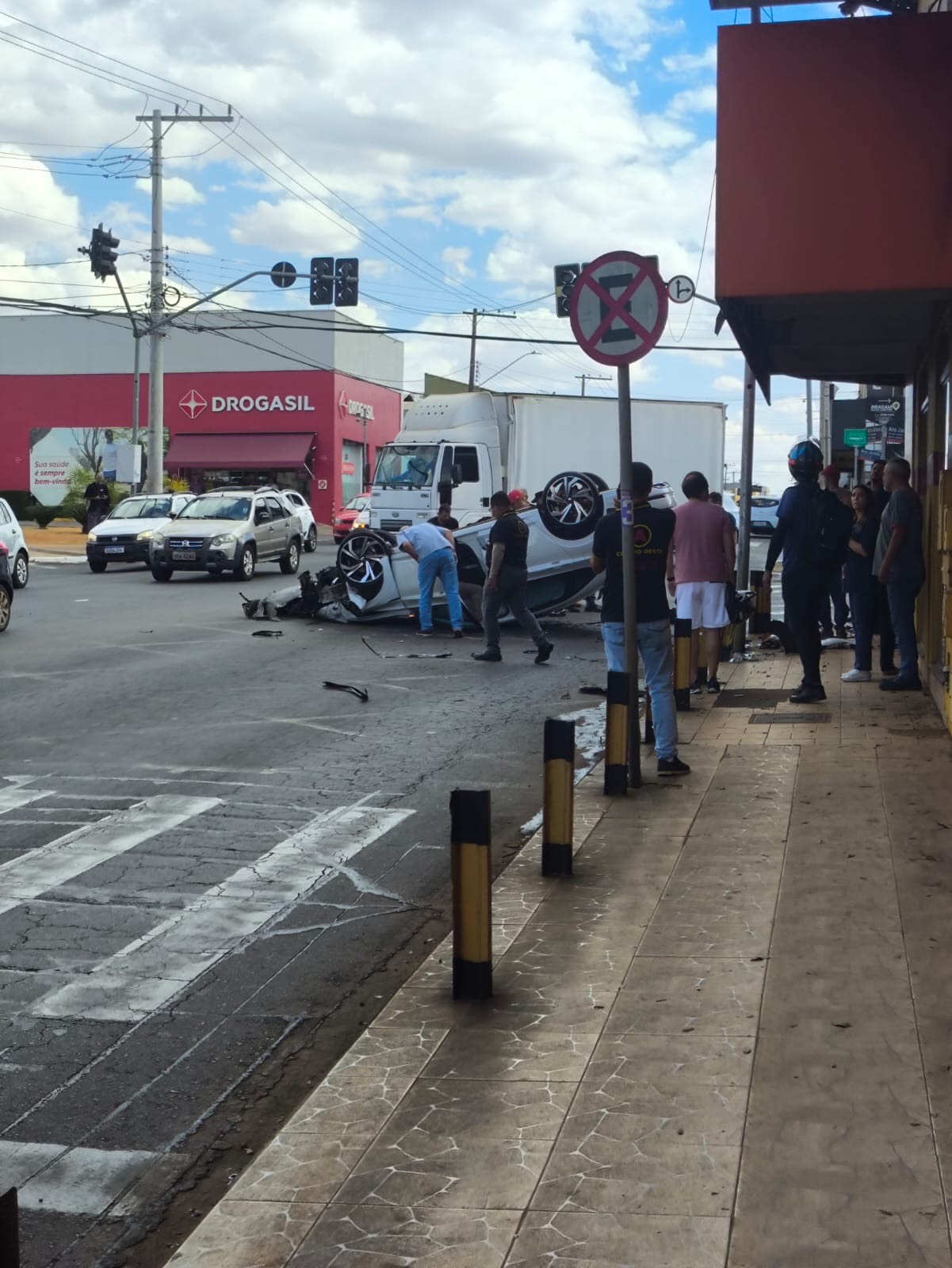 Imagem veiculo capotada na avenida, pessoas estão próximas ao carro