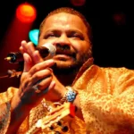 Imagem cantor Arlindo Cruz, ele está batendo palmas em frente o microfone