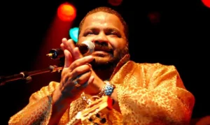 Imagem cantor Arlindo Cruz, ele está batendo palmas em frente o microfone