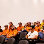 Imagem homens com camiseta laranja do grupo legendários, eles estão sentados e com boné na cabeça