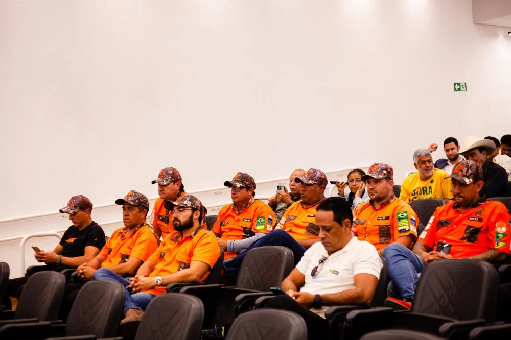 Imagem homens com camiseta laranja do grupo legendários, eles estão sentados e com boné na cabeça