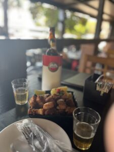 Imagem Cerveja e tira gosto no bar, uma garrafa de cerveja e dois copos pela metade no meio uma porção de torresmo com mandioca