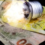 Imagem lâmpada de luz em cima de duas notas, uma de vinte e outra de cinquenta reais