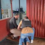 Imagem policiais prendendo elemento, o homem está no chão deitada e os dois policiais estão agachados efetuando a prisão