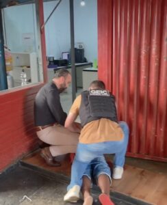 Imagem policiais prendendo elemento, o homem está no chão deitada e os dois policiais estão agachados efetuando a prisão