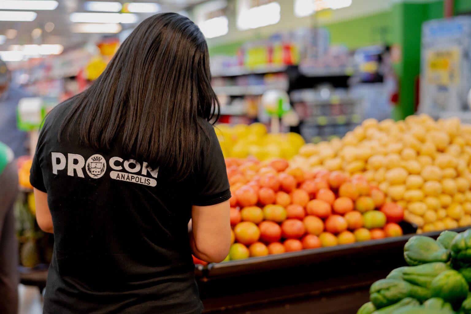 Imagem mulher com camisa preta do Procon na frente tem tomate, batata, chuchu