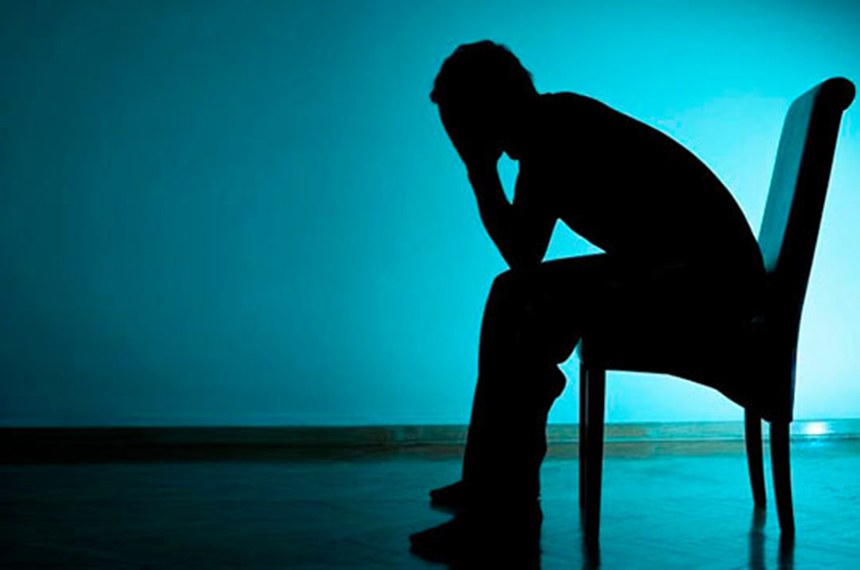 Imagem toda escura, tipo sombra, de uma pessoa sentada em uma cadeira com as duas mãos na cabeça