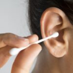 Imagem mão segurando um cotonete em direção ao ouvido