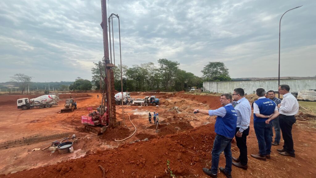 Imagem homens observam canteiro de obras, onde estão maquias e caminhões
