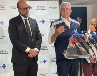 Imagem entrevista coletiva Ministro da Saúde, ele está de colete azul com vários microfones a frente