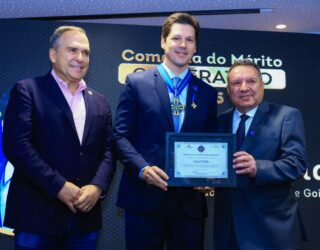 Imagem Daniel Vilela segura uma placa de homenagem ladeado por duas pessoas