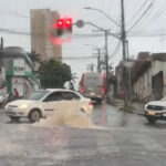 Imagem bueiro jorrando agua, carros passam ao lado