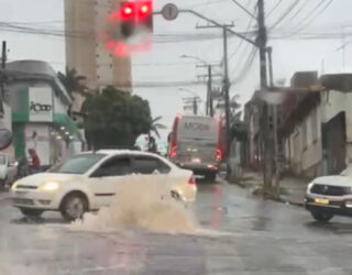 Imagem bueiro jorrando agua, carros passam ao lado