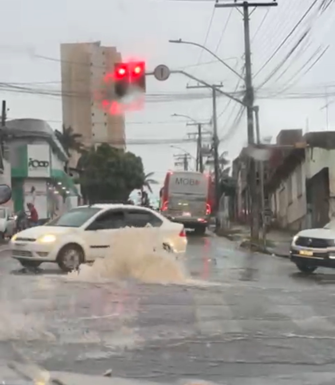 Imagem bueiro jorrando agua, carros passam ao lado