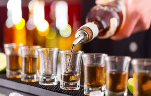 Imagem bebida sendo colada em copos, garrafa com liquido amarelo enche os copos que estão um ao lado do ouro