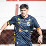 Imagem jogador em campo, com uniforme azul claro, dominando a bola de jogo
