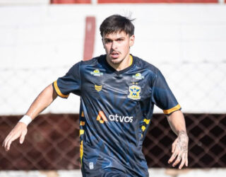 Imagem jogador em campo, com uniforme azul claro, dominando a bola de jogo