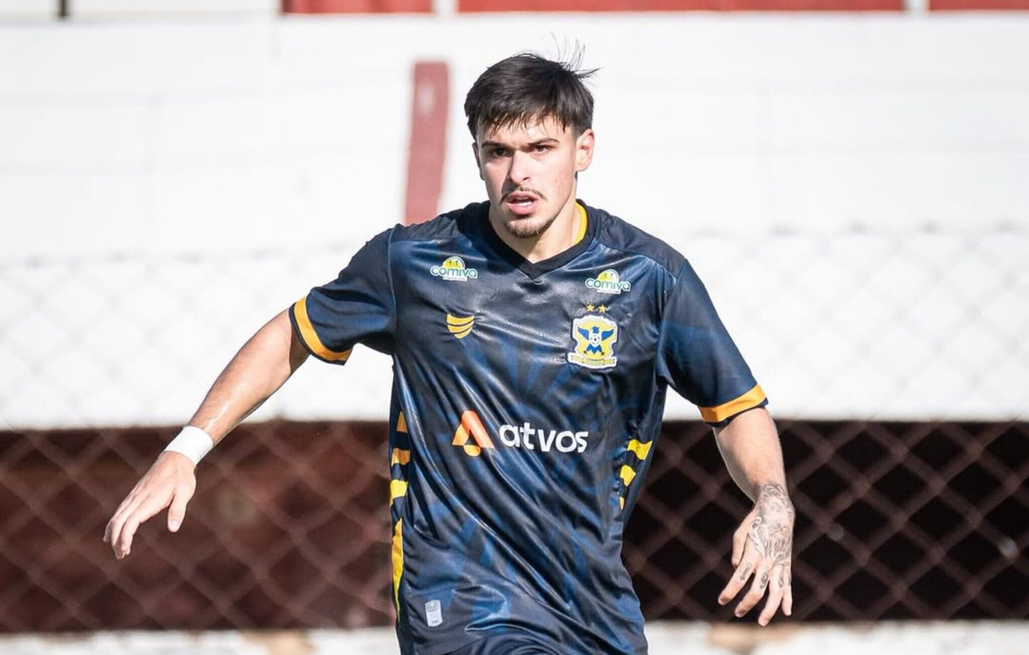 Imagem jogador em campo, com uniforme azul claro, dominando a bola de jogo