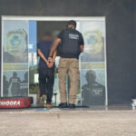 Imagem policial conduzindo homem algemado