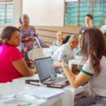 Imagem pessoas atendidas do outro lado pessoas atendendo sentadas atrás de uma mesa