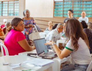 Imagem pessoas atendidas do outro lado pessoas atendendo sentadas atrás de uma mesa