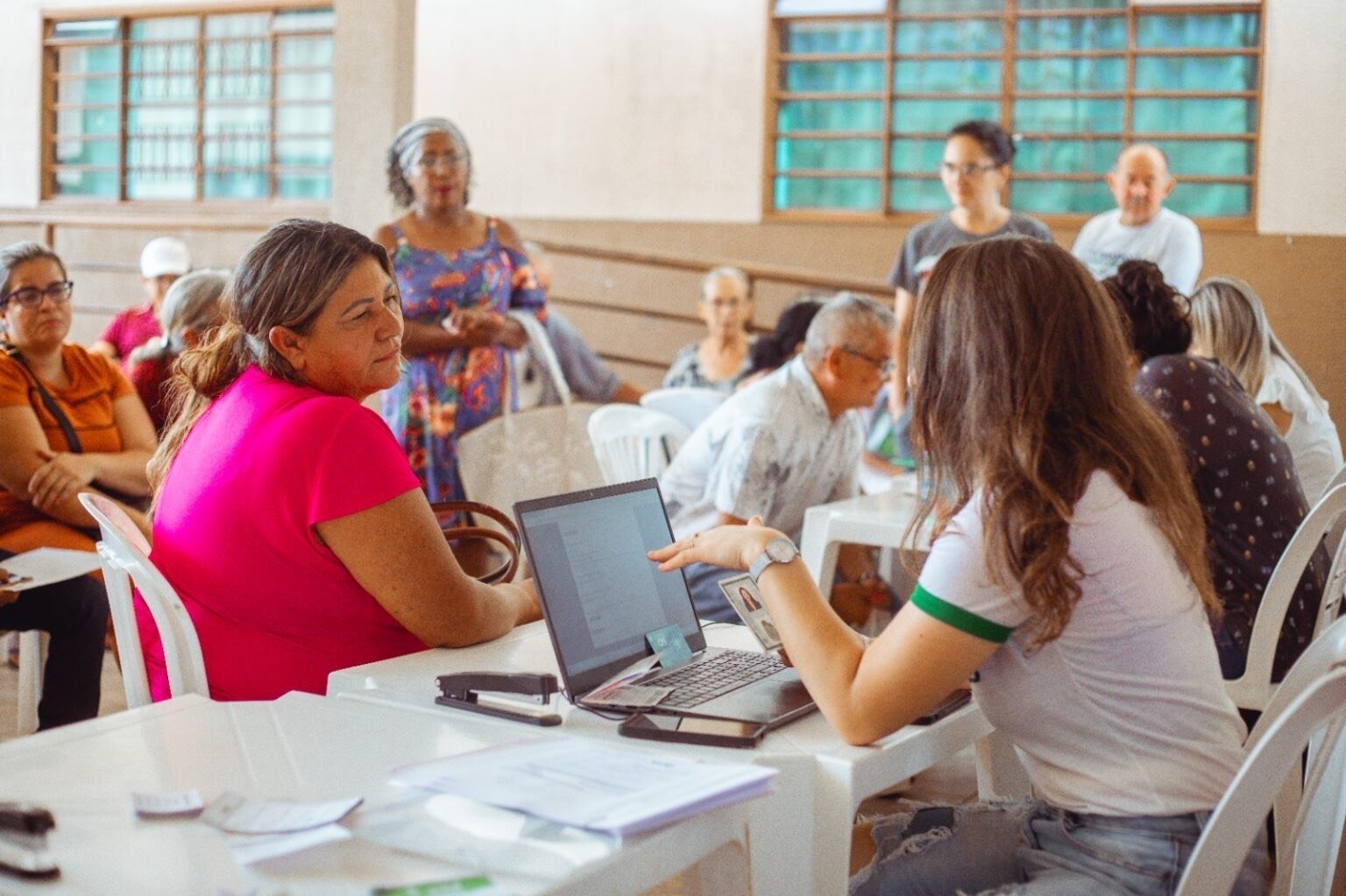 Imagem pessoas atendidas do outro lado pessoas atendendo sentadas atrás de uma mesa
