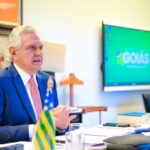 Imagem homem sentado na mesa olhando para frente, ele está de terno azul e gravata cor de rosa