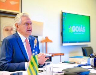 Imagem homem sentado na mesa olhando para frente, ele está de terno azul e gravata cor de rosa